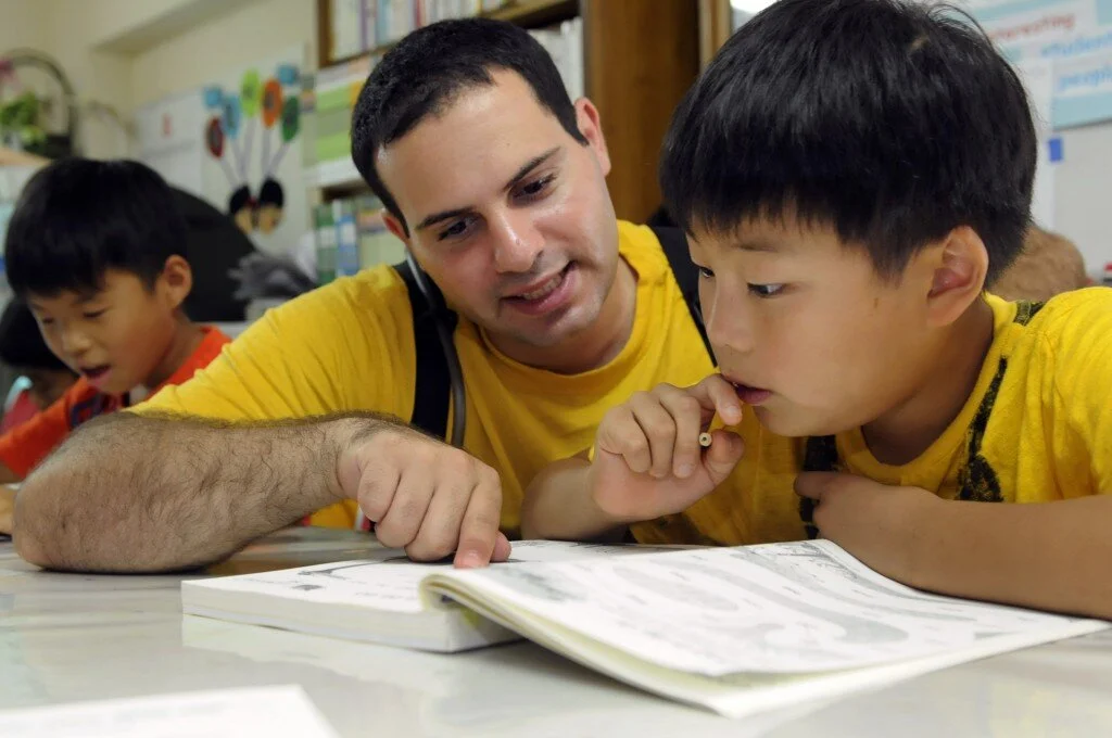 A teacher helping a student read in an ESL classroom